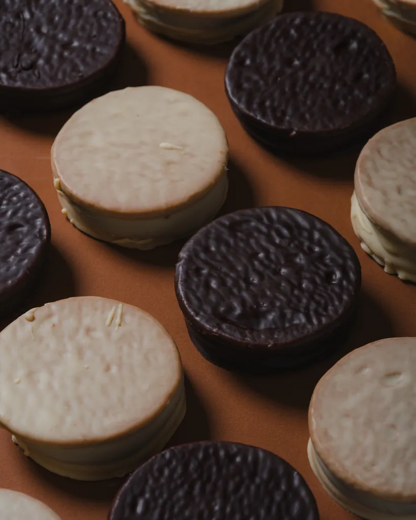 Alfajores Malfatti de chocolate negro y de chocolate blanco vistos desde arriba, ordenados sobre un fondo naranja.